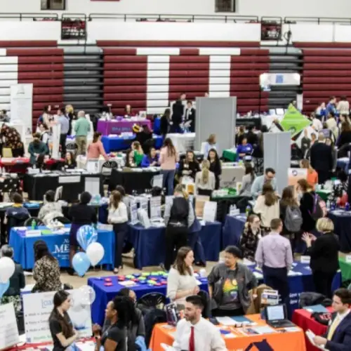 Dozens of university's representatives with tables and banners fill a gymnasium with crowds of people