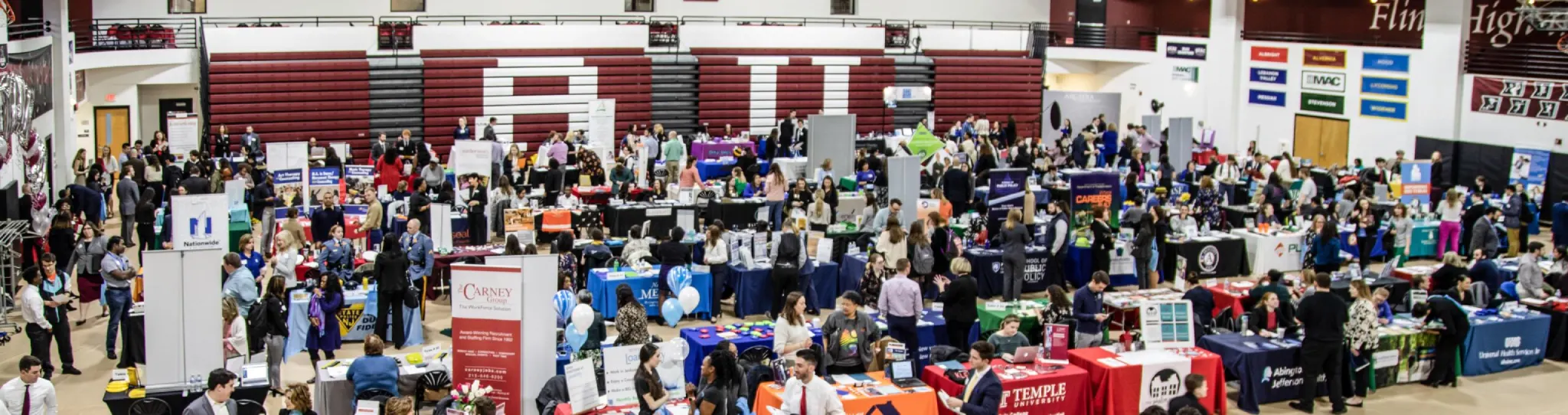 Dozens of university's representatives with tables and banners fill a gymnasium with crowds of people