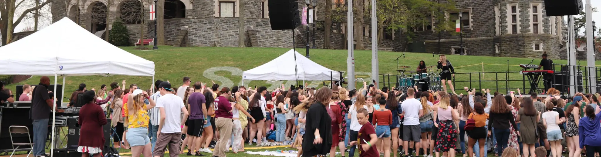 A large crowd standing in front of a stage, listening to the performer.