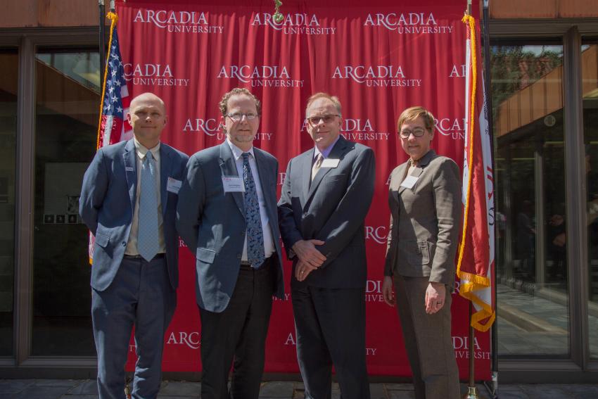 Four Arcadia leadership team members pose in front of the Arcadia banner with flags at each end.