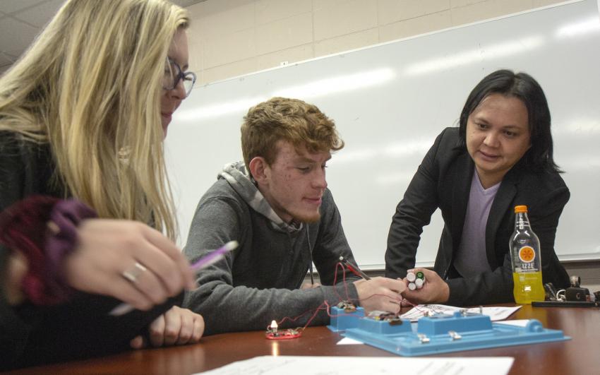 A professor leans over a table while two students work on an experiment