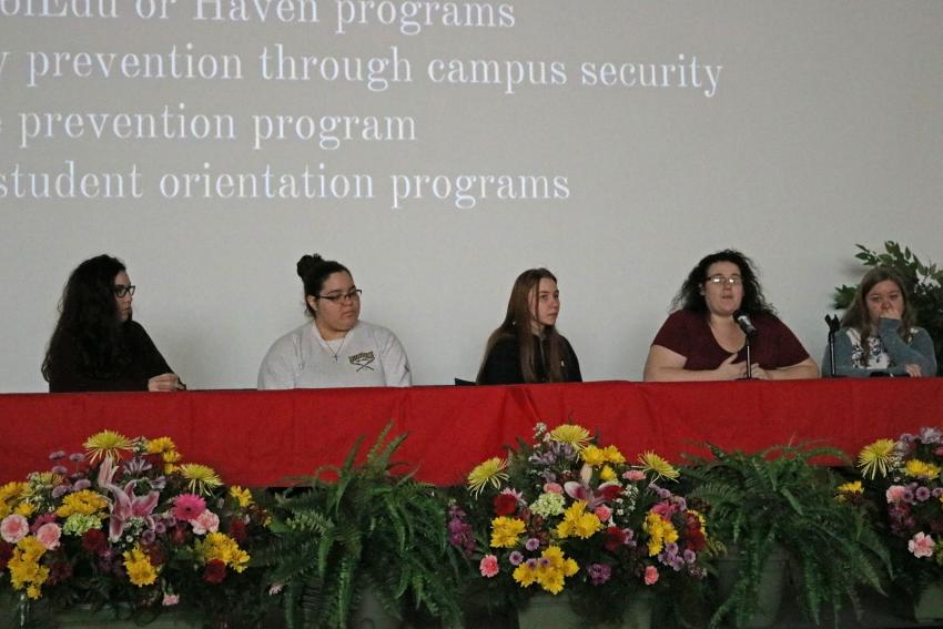 Five women on a panel with a large screen behind them.