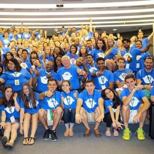 A diverse group of students in blue shirts fill an auditorium style classroom