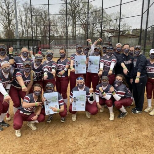 Women's softball team posing for a picture, holding up signs and wearing green bands.