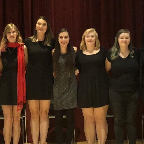 A group of female students on a theater stage dressed in black and red.