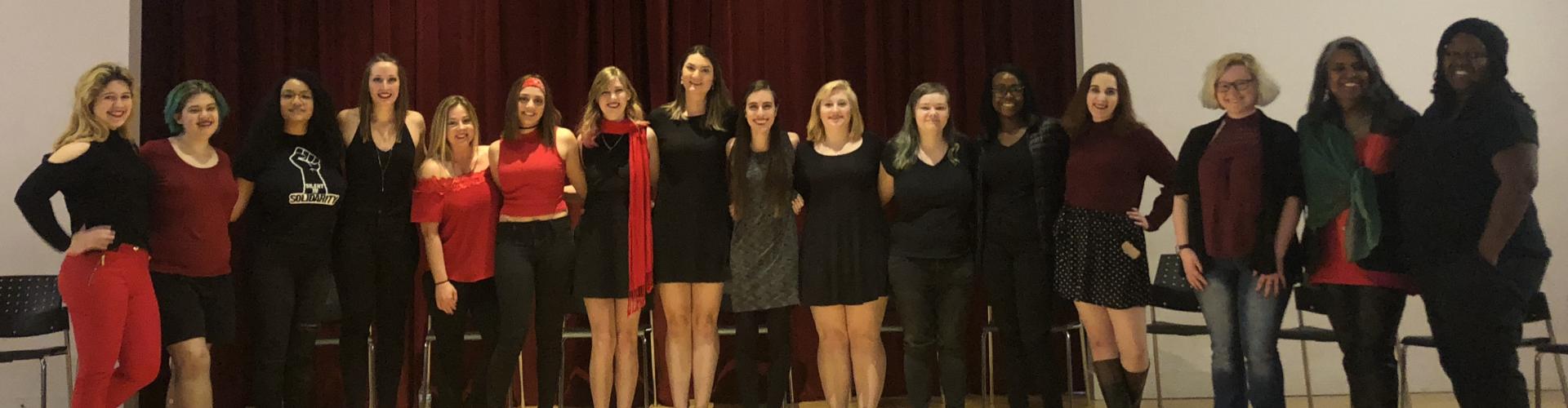 A group of female students on a theater stage dressed in black and red.