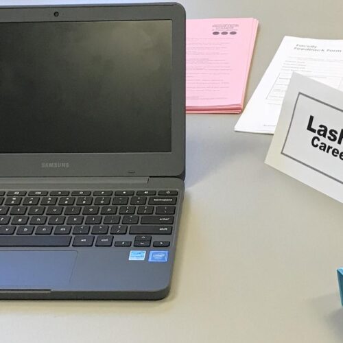 A desk area with a laptop, career prep papers, and name tag of Lashana Bryant, Career Peer Advisor