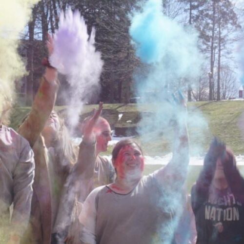 Students throw holi color powder into the air.