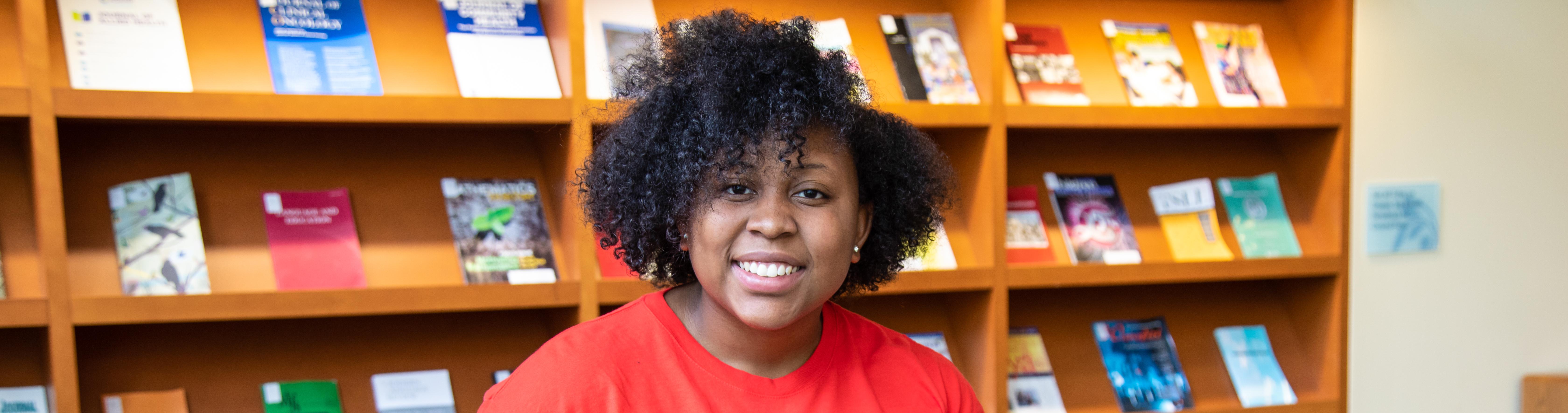 A woman sitting with a bookcase behind her