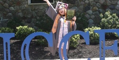 A graduate standing in front of a blue "SUCCESS" sign