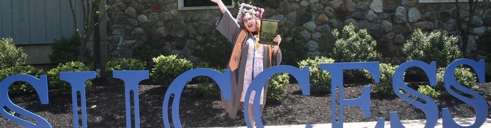 A graduate standing in front of a blue "SUCCESS" sign