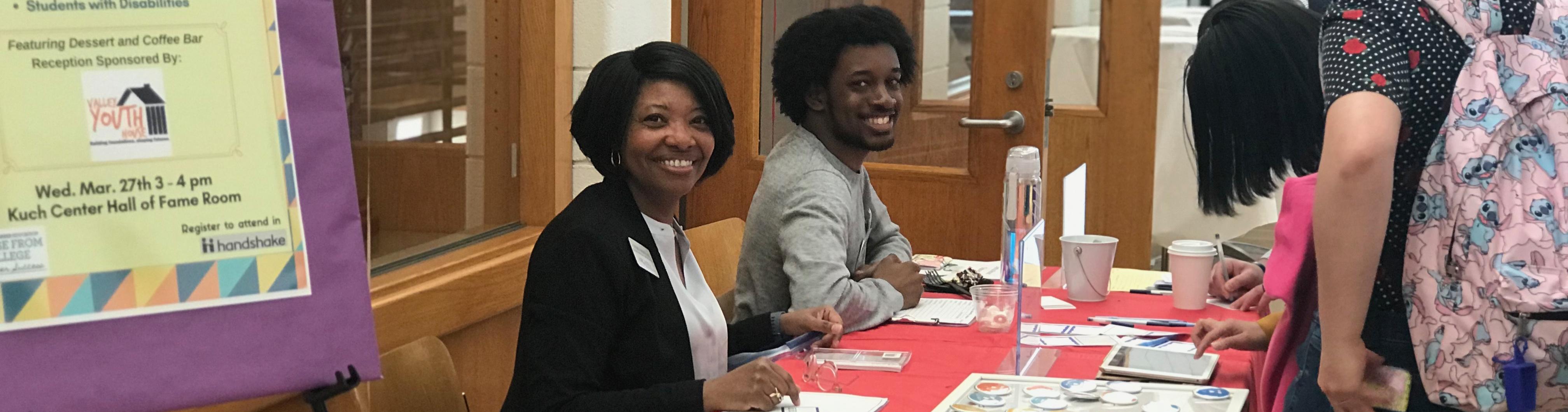 Two people smiling at the camera sitting down at a table