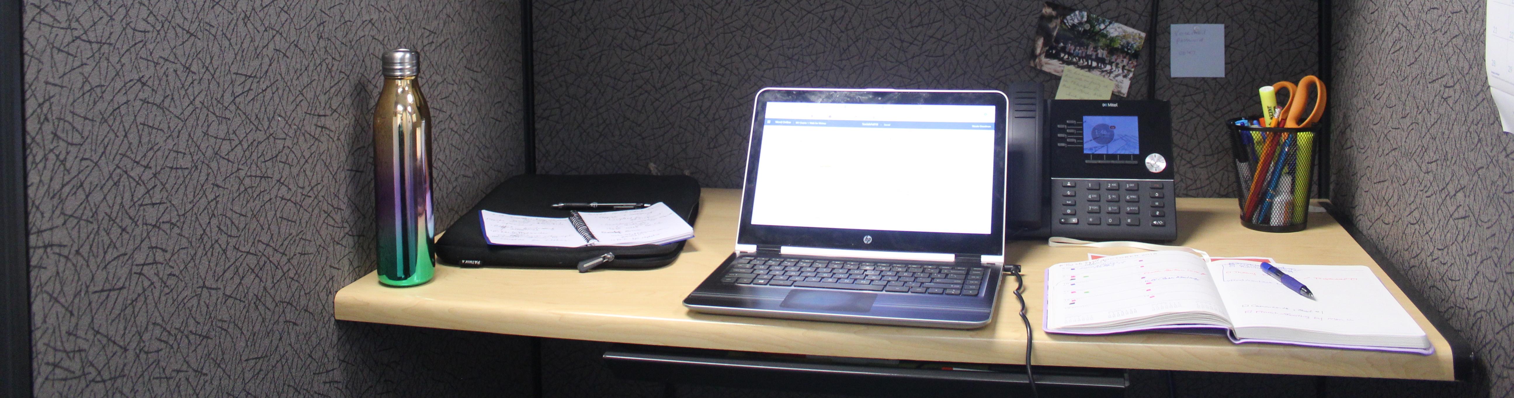 Cubicle desk with laptop and other office items.