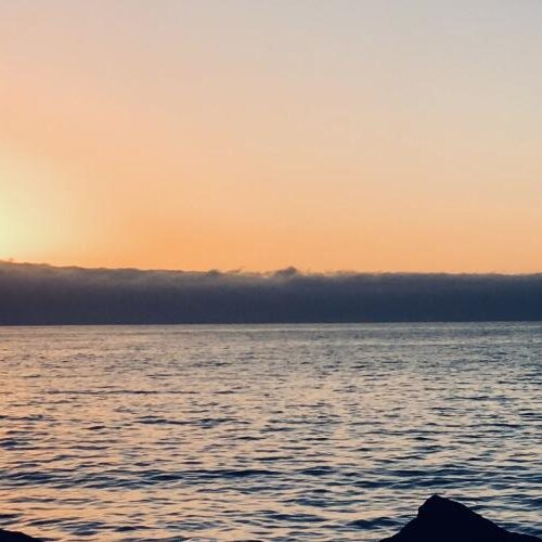 A student studying abroad in front of a body of water while the sun sets