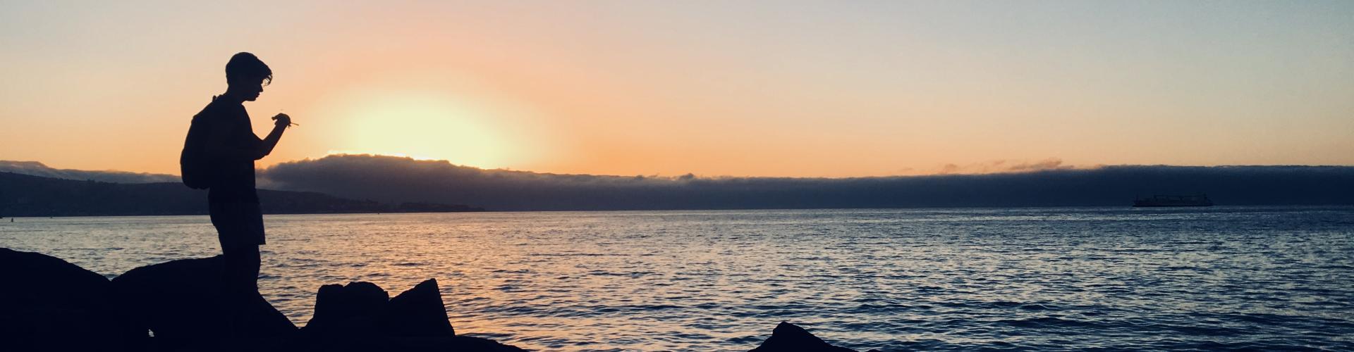 A student studying abroad in front of a body of water while the sun sets