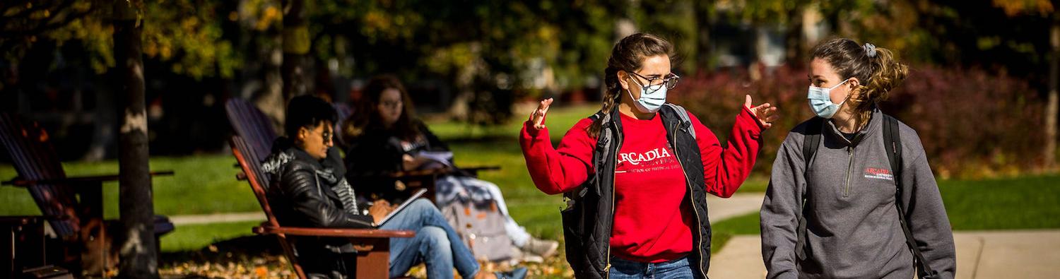 Two students wearing face masks talk to each other while walking on the Walk of Pride