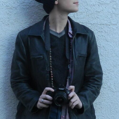 A person leaning against the wall carrying a Canon camera in their hands