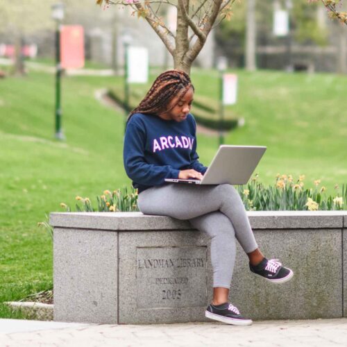 Photo of students sitting outside on campus talking, studying, and on their computers.