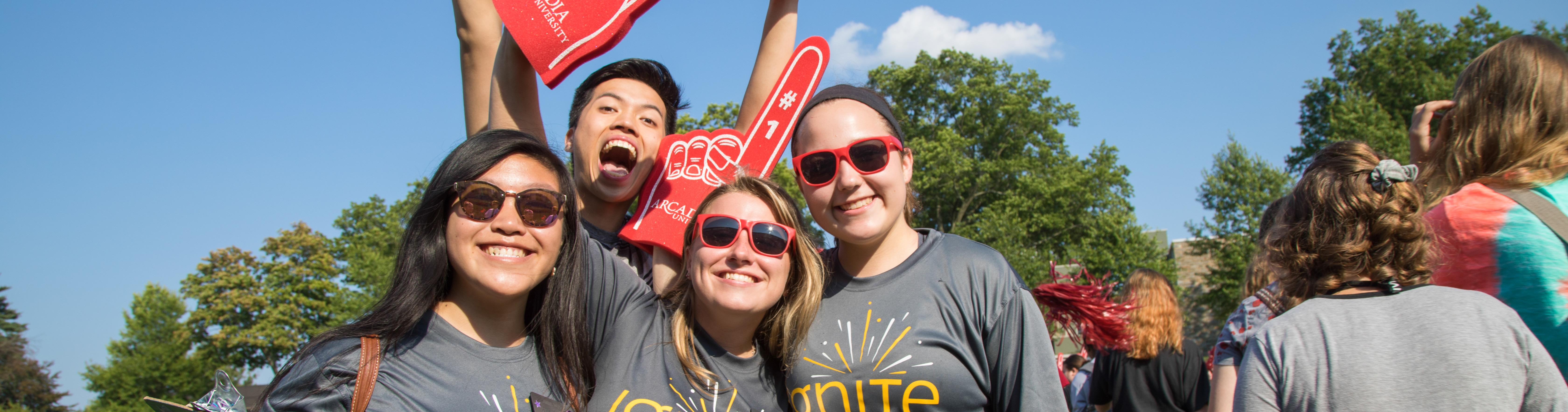 Four students wearing grey "Ignite" t-shorts and holding Arcadia foam fingers