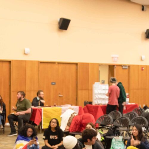 A woman speaking at a microphone in the Great Room to students and faculty.