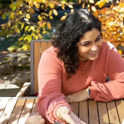 Three students sit together at a table outside of Commons with yellow fall leaves on the tree behind them