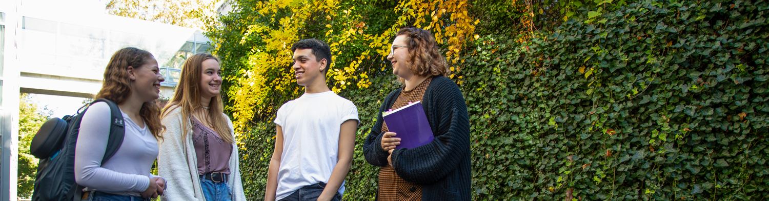 Photo of four students standing outside Easton Hall talking and laughing.