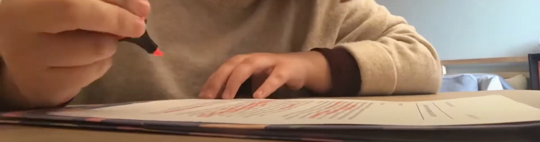 A student's hand holds a pink highlighter above a printed piece of paper.