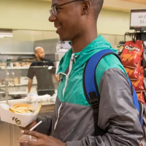 Two students smile at each other while holding food, a food counter behind them