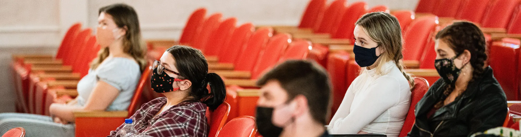 Students sit distanced and masked in an auditorium classroom