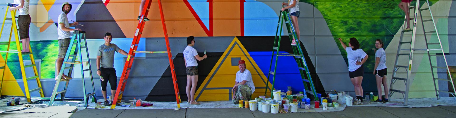 Students paint a mural multi colors as part of Bridging Connections