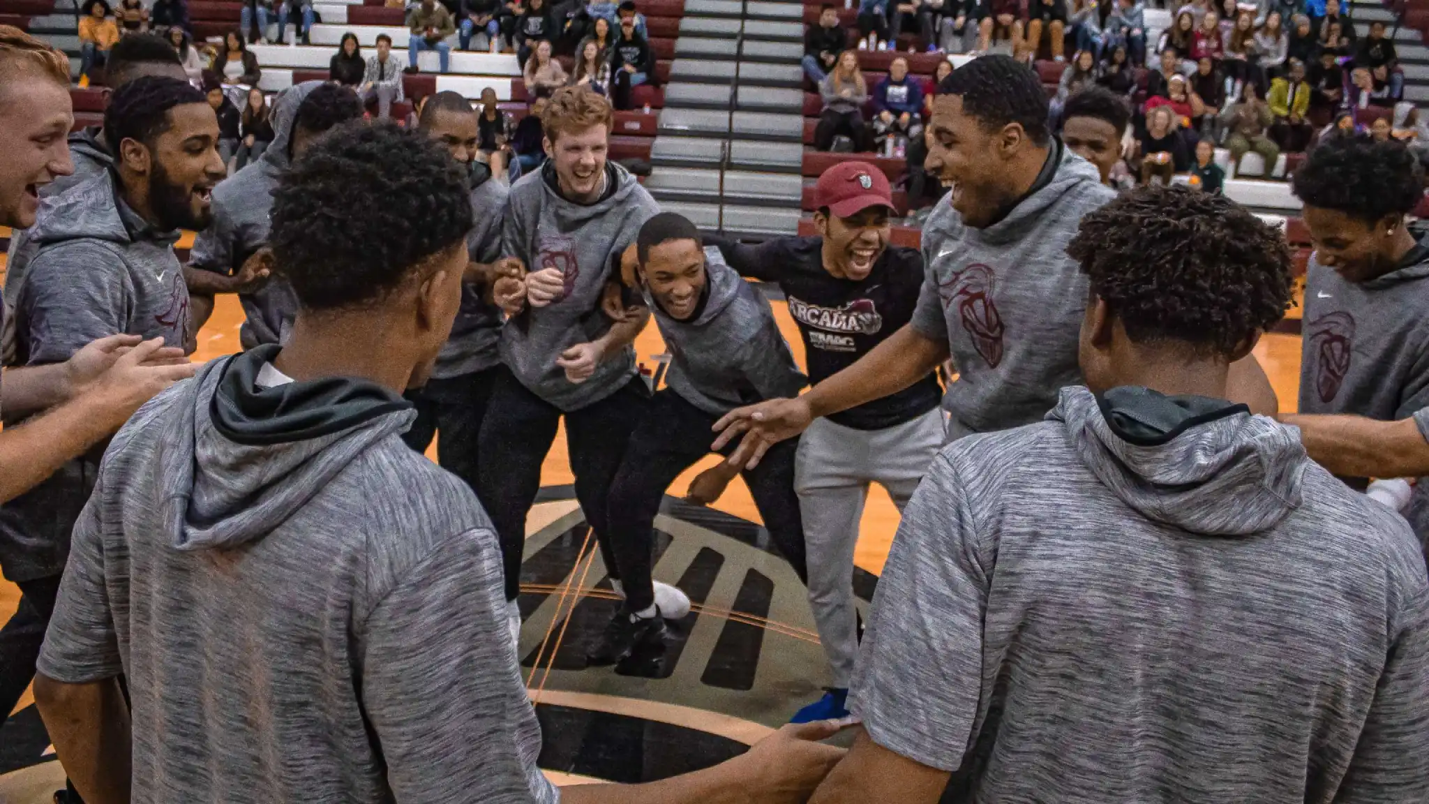 Group of excited student athletes in circle on basketball court during Knight Madness