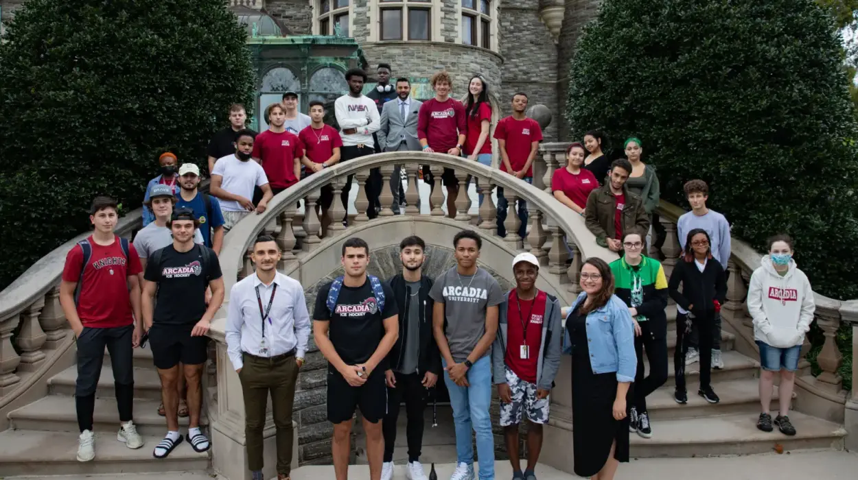 Group of students stand together on campus and smile at the camera.