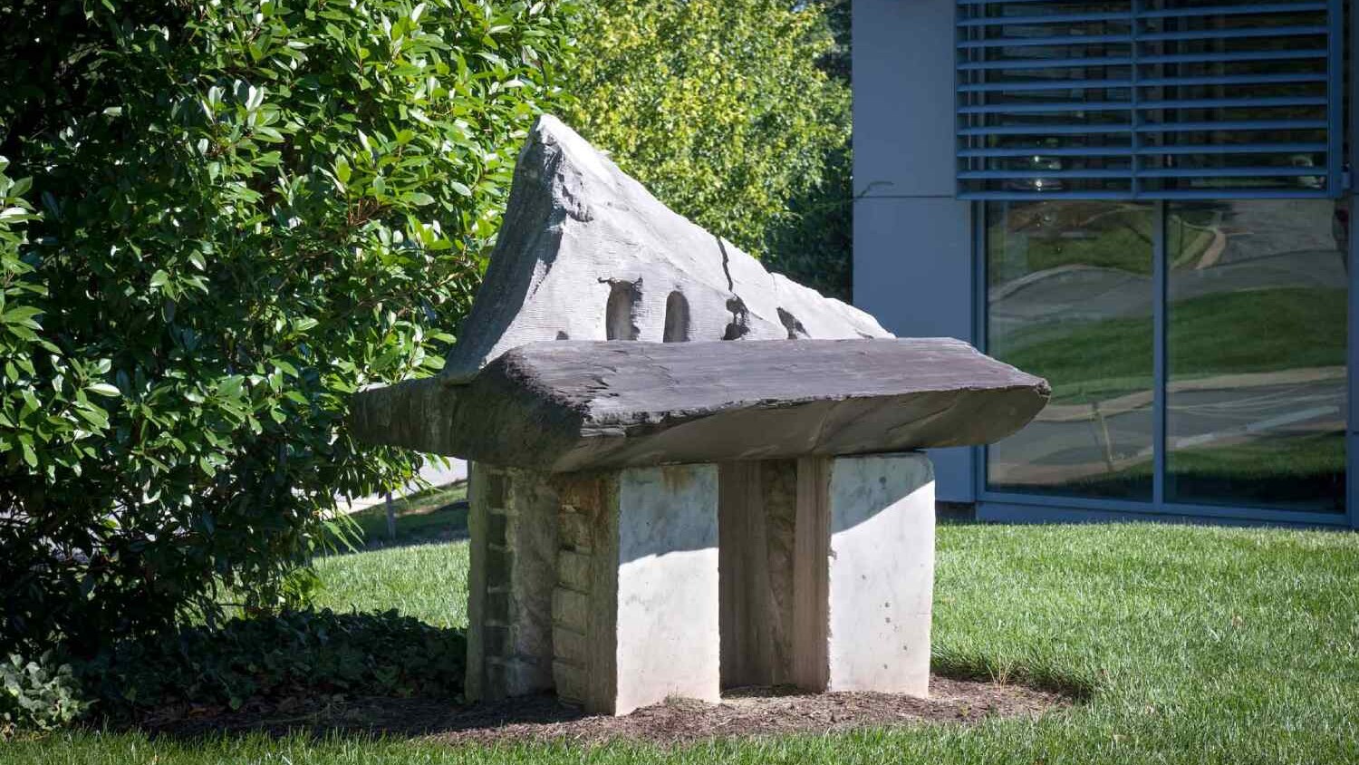 a large stone sculpture with a tree and a building in the background