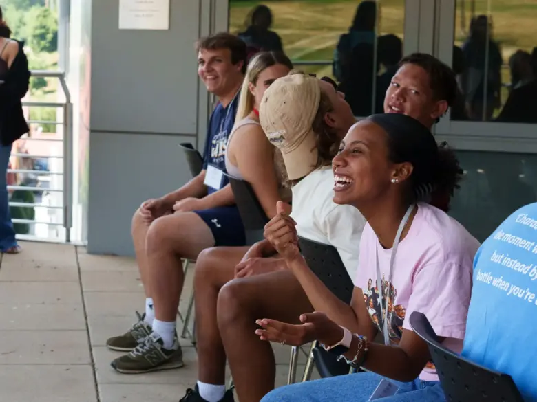 Students laughing and sitting in chairs outside during orientation