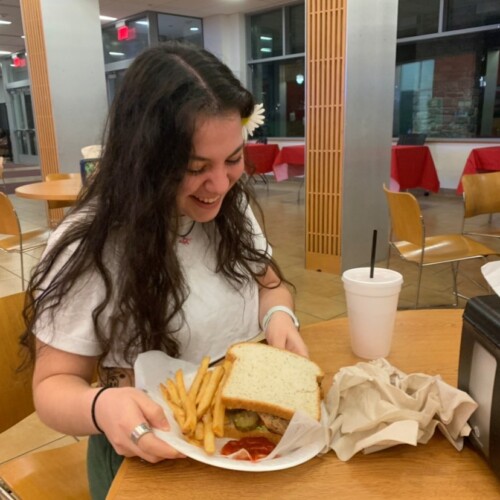 A student smiling while looking at her sandwich and french fries