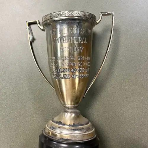 An aged silver trophy is engraved with "President’s Cup Intramural Riflery Trophy dating from 1938-1948."