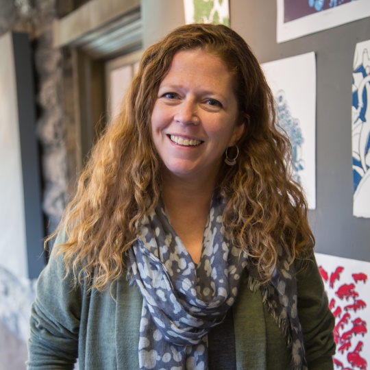 Carole Loeffler stands and smiles outside a classroom at Arcadia University