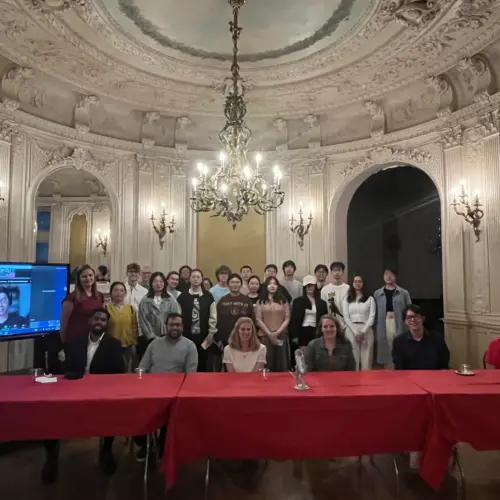 Six Arcadia alumni are seated at tables with a group of current students standing behind them