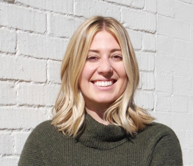 The headshot of a blonde woman in dark green sweater.