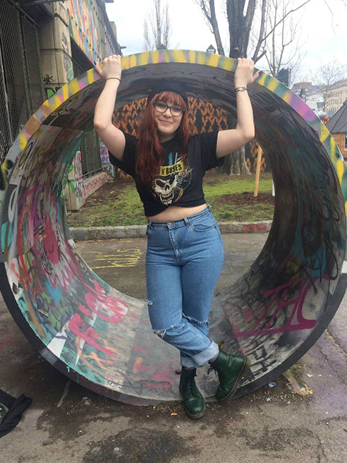 Arcadia student, Kat Bleiweiss, stands in a consrtudtion park covered with graffitti.