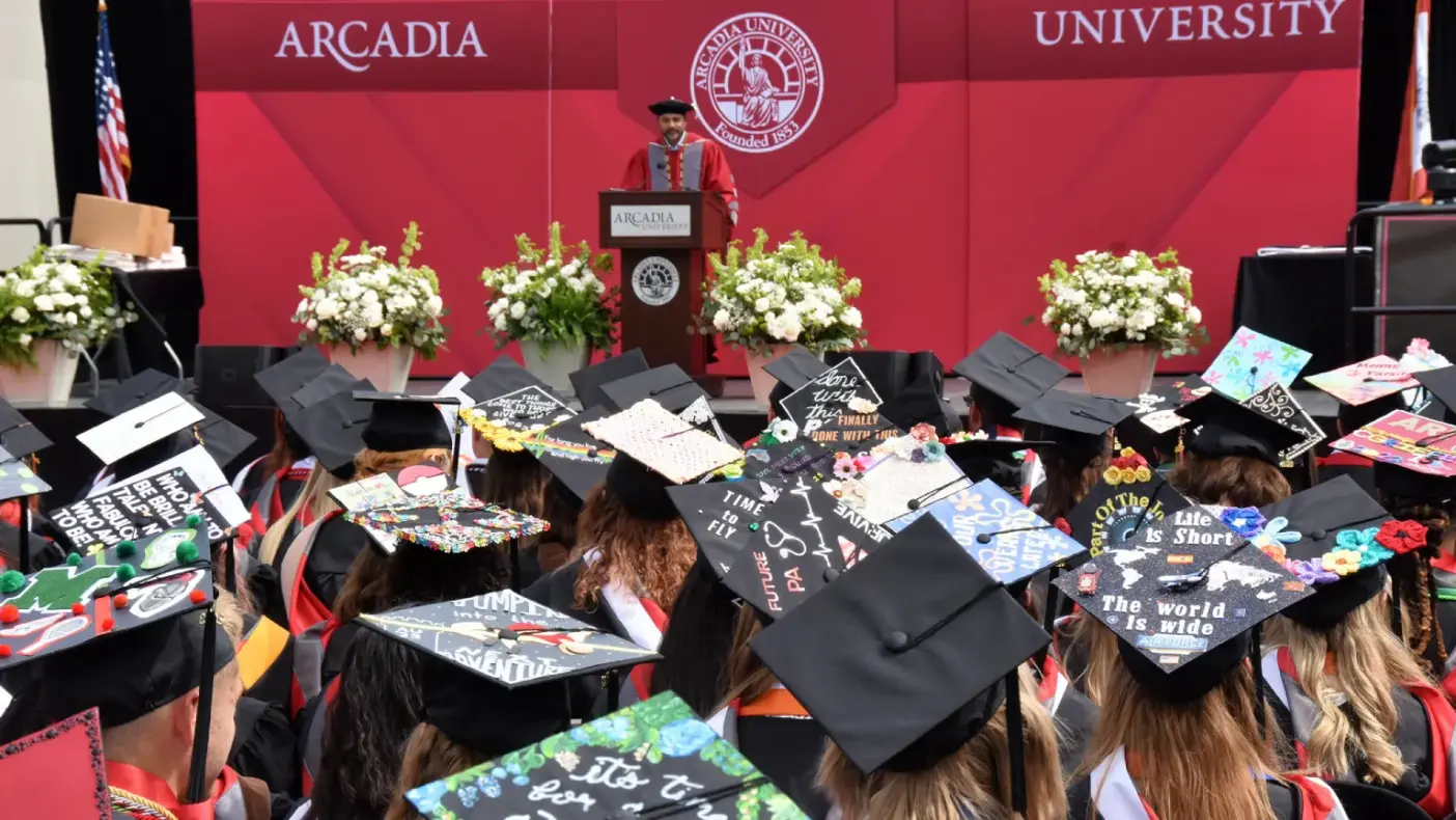 President addresses undergraduates seated and wearing their cap and gowns.