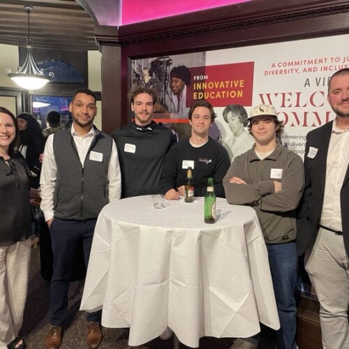 Female Professor standing with Five Alumni in the Welcome Center in the Castle.