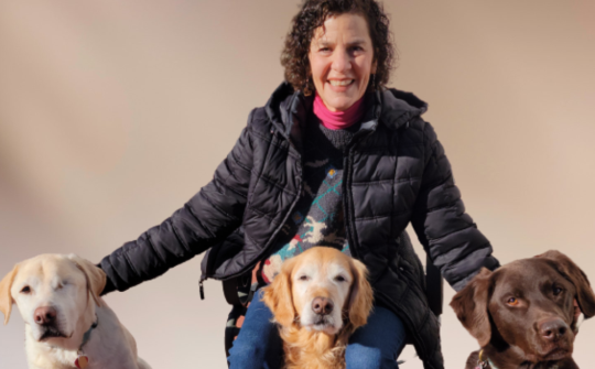 Alumna smiling with her three rescue dogs around her.