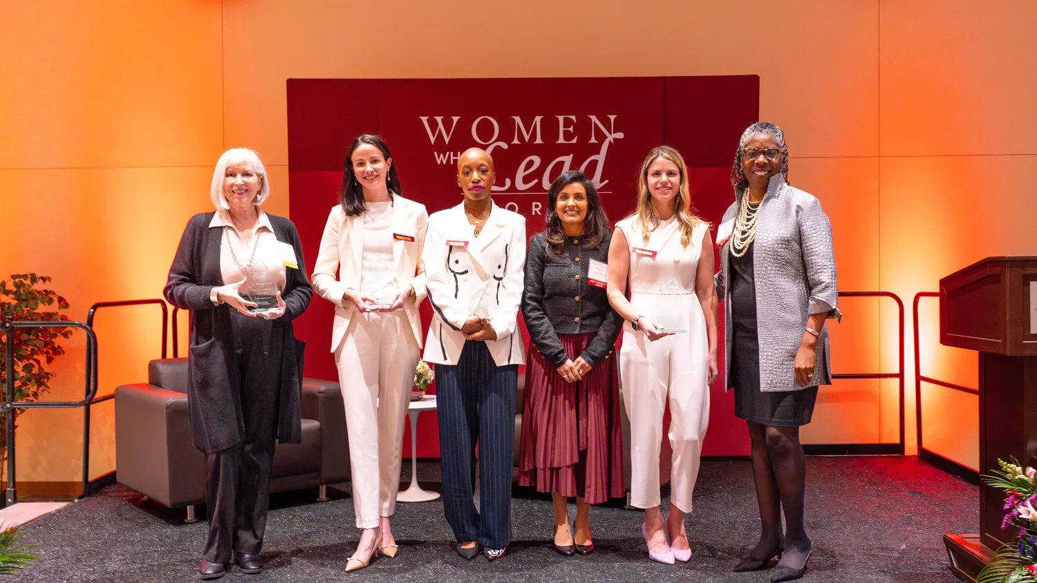 Six women stand in font of a Women Who Lead Forum 2024 at Arcadia University sign during the event.