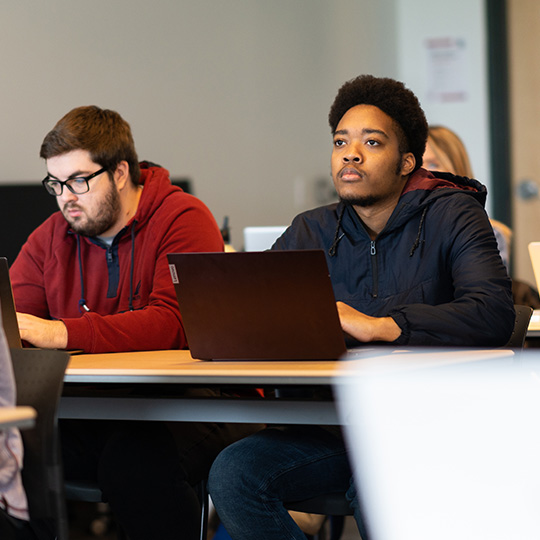 Students sit at their desks and listen during class at the School of Global Business.