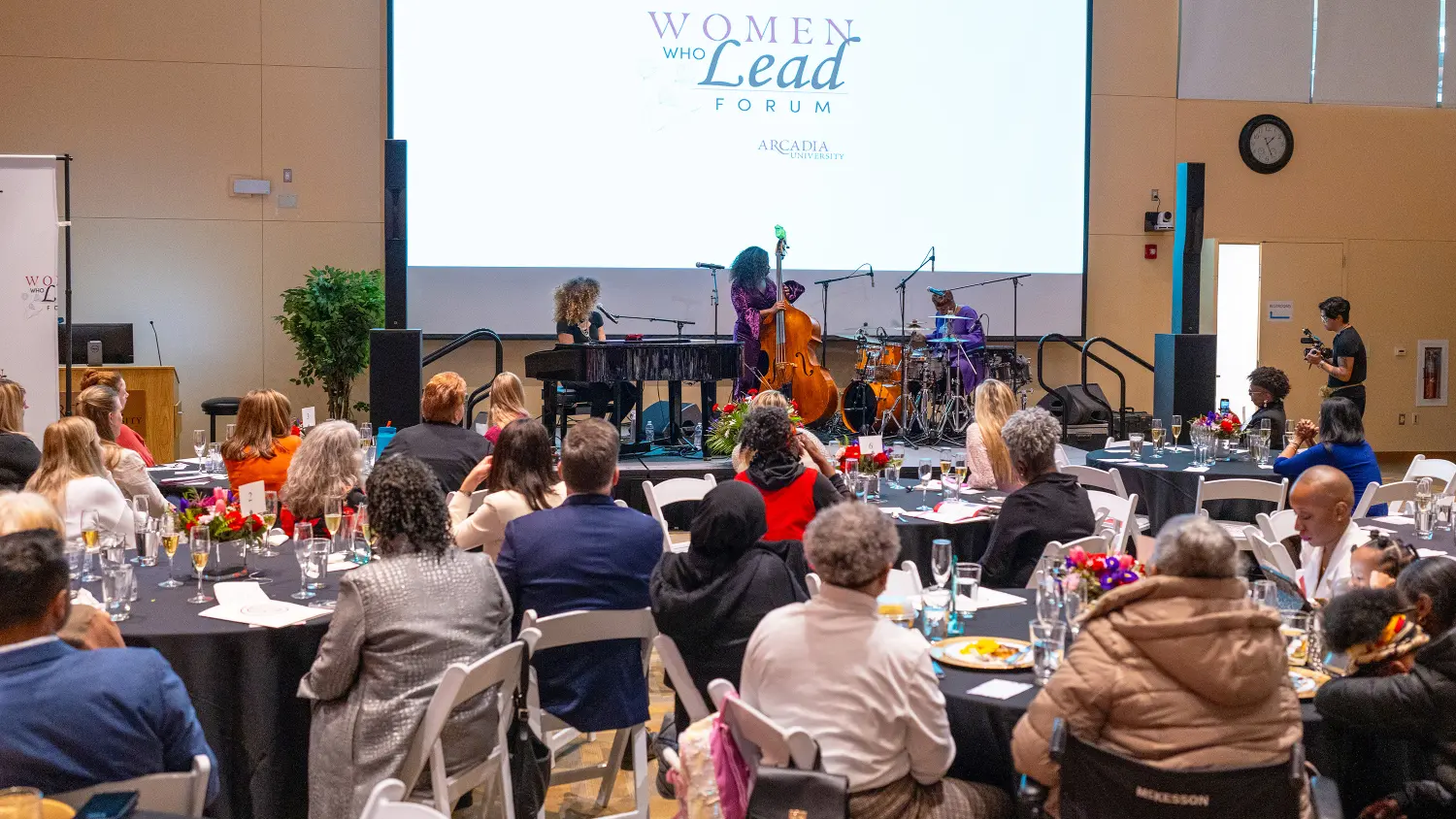 A crowd sits at luncheon table by a screen during the Women Who Lead Forum 2024 event.