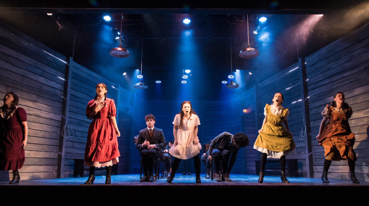 Several actors standing and singing on stage