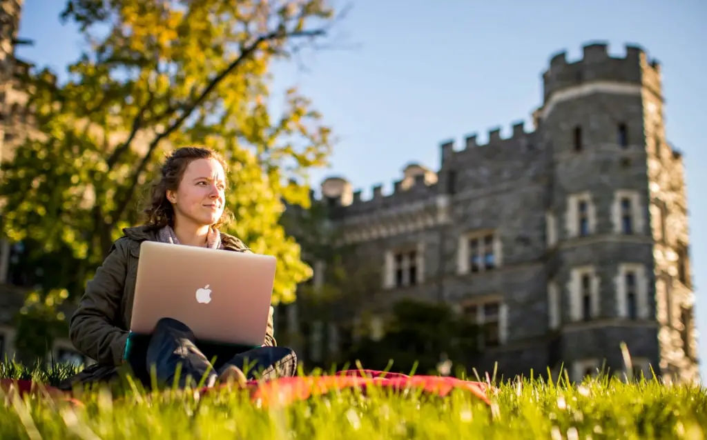 female students sitting in front of The Csatle on her laptop