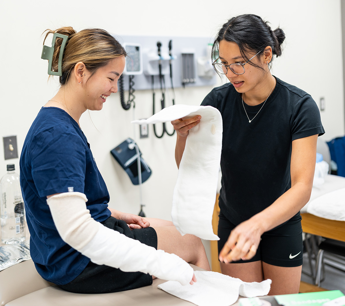 Two PA students practice setting a bandage on an arm in a clinical classroom.