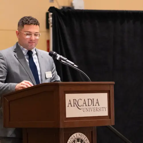 man in suit standing behind Arcadia University branded podium in the Kuch Center during the Athletic Award Event